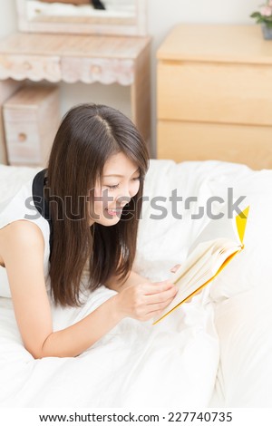 young attractive asian woman who reads a book in bed