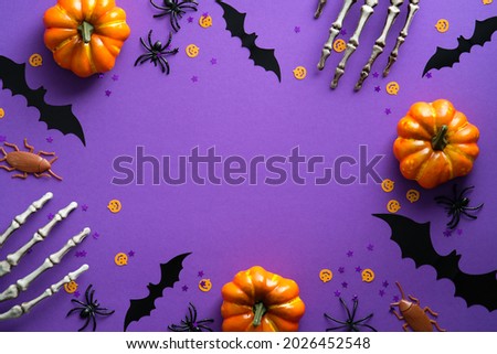 Happy Halloween holiday concept. Halloween decorations, skeleton hands, bats, pumpkins on purple background. Halloween party greeting card mockup with copy space. Flat lay, top view, overhead.
