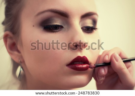 Make-up artist applying lipstick with a brush on model's lips, close-up
