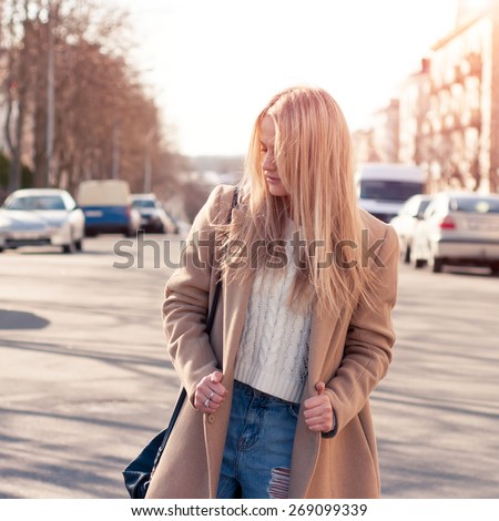 Amazing blonde girl walking alone on the road in old european city. Dressed on ripped jeans and coat