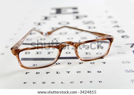 horn rim readingglasses sitting on top of an eye exam chart, foreground sharp and background soft