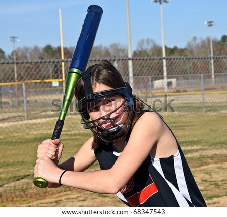 A young softball player with safety equipment on ready to hit the ball.