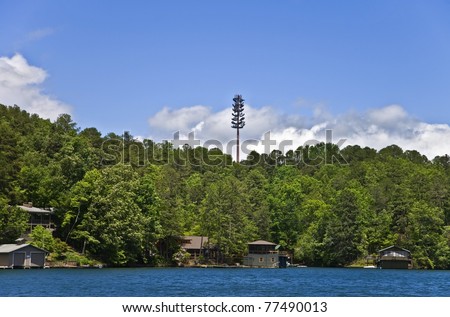 A cell tower high above the tree line over homes and a lake.