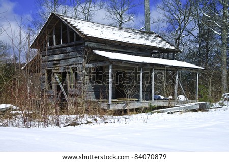 An abandoned house in the winter surrounded by deep snow and a beautiful blue sky.