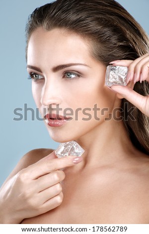 Beautiful woman applying ice cube treatment on blue background