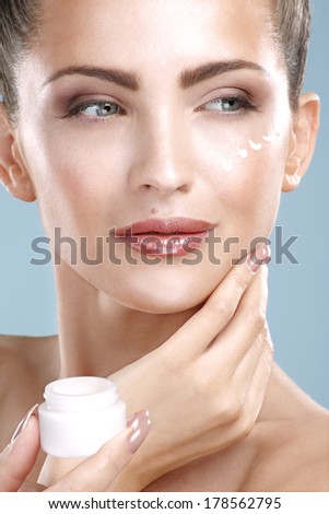 Beautiful woman applying cream treatment on her perfect face on blue