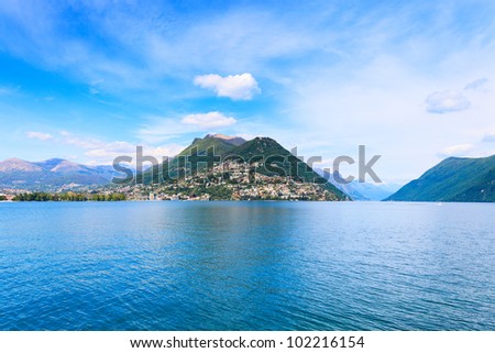 Lugano Lake landscape. City, lake water, blue sky and mountains. Ticino, Swiss or Switzerland, Europe.