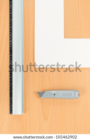 Handheld mat cutter kit. Cutting metric rule guide, mat knife and white mat on wooden background
