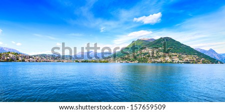 Lugano Lake panoramic landscape. City, lake water, blue sky and mountains. Ticino, Swiss or Switzerland, Europe.
