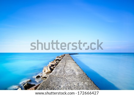 Concrete and rocks pier or jetty on a blue ocean water. Long Exposure photography