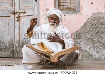 Close up of an old indian sadhu (saint) sitting and reading sacred texts near the temple.