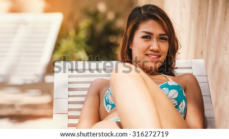 Beautiful happy young Asian Sexy woman sitting in blue bikini next to swimming pool, looking at camera.
