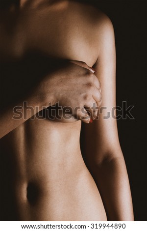 Close up portrait of a topless Asian sexy woman covering her breast with hand isolated over black background.