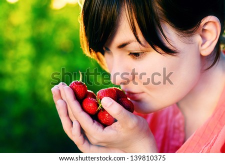 Caucasian woman with strawberries in hands without makeup at green nature background outdoors