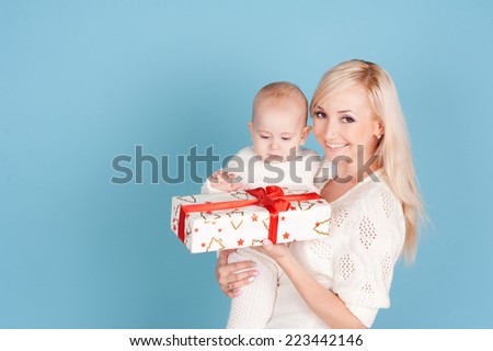Smiling woman holding baby boy with christmas gift over blue. Happy family portrait