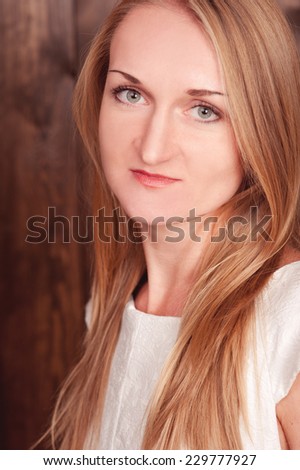 Smiling blonde woman posing over wooden wall. Young girl 20-25 years old looking at camera.