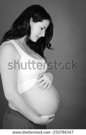 Black and white image of pregnant woman holding her belly in room. Motherhood.