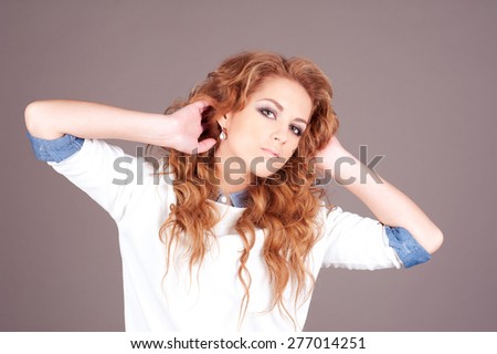 Portrait of young girl 20-24 year old posing in room over grey. Long curly hair. Elegance.