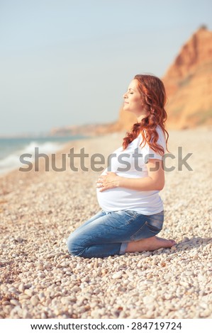 Pregnant woman resting at seashore. Wearing casual clothes outdoors. Motherhood. Maternity.