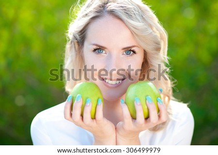 Smiling blonde girl 20-24 year old holding green apples at nature background. Healthy eating, 20s. Looking at camera.