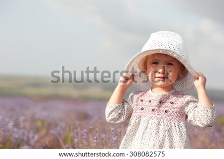 Stylish baby girl 2-3 year old walking in lavender field. Wearing rustic dress and hat. Looking at camera.