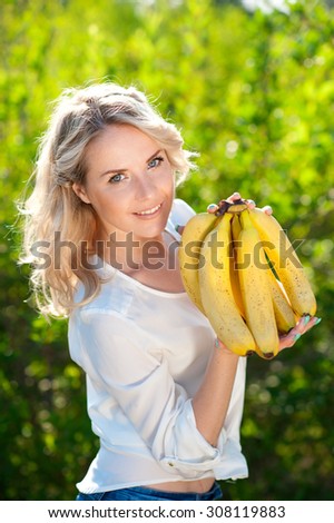Smiling girl holding bundle of bananas outdoors. Looking at camera. Healthy lifestyle. Organic food.