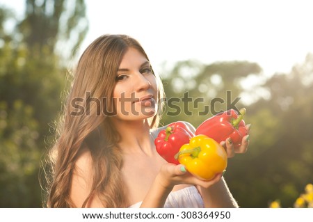 Young woman 20-24 year old holding raw peppers outdoors. Looking at camera. Fall season. Harvesting.