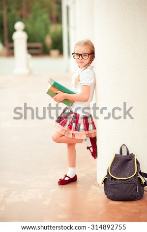 Cute kid girl standing with books and school bag in park. Looking at camera. Childhood. Back to school.
