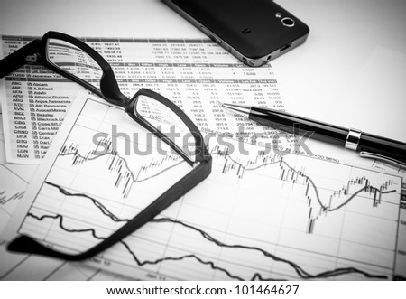 data analyzing in stock market: on the charts and quotes prints, the smart phone, eyeglasses and a pen