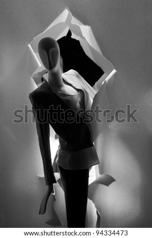 a female mannequin dressed the highlighted in a shop window decorated by torn like paper in grayscale