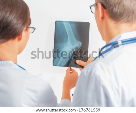Two doctors look at x-ray picture of the knee joint, rear view. Point of view shot
