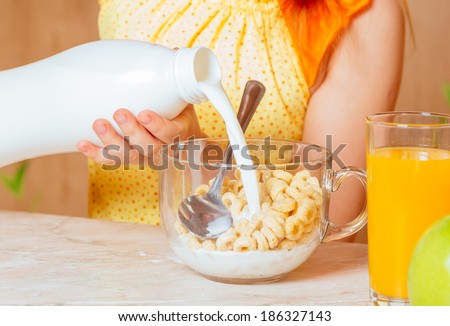 Little girl pours milk in cereal flakes for breakfast, face is not visible