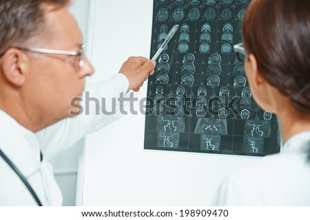 Senior doctor examines MRI image of human head. Older man doctor teaches young woman doctor