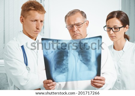 Older man doctor and young doctors examine x-ray image of lungs in a clinic