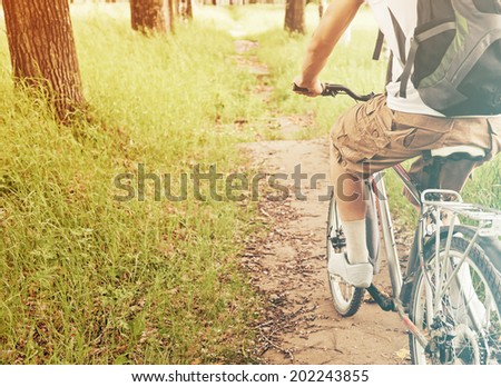Unrecognizable man is riding bicycle on path in summer park. With sun Light effect