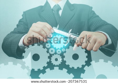 Unrecognizable businessman holds calipers with cogwheels, concept of business creation
