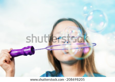 Little girl is blowing soap bubbles on background of blue sky. Focus on soap bubble.