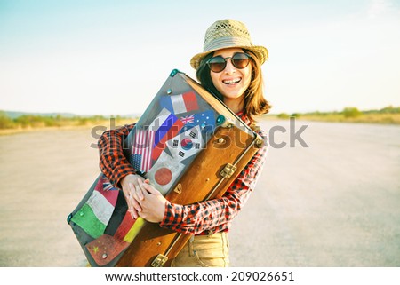 Happy woman traveler embraces a vintage suitcase on road. Suitcase with stamps flags representing each country traveled.
