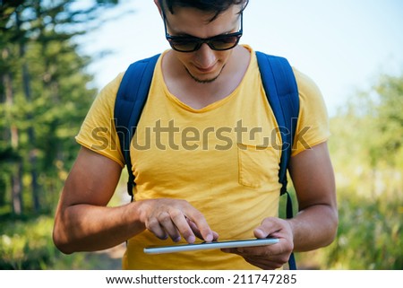 Tourist young man searches something on tablet PC in the forest