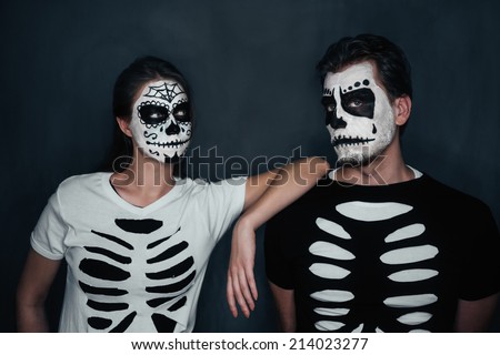 Loving couple with skull face art in costume of skeletons on dark background, Halloween theme