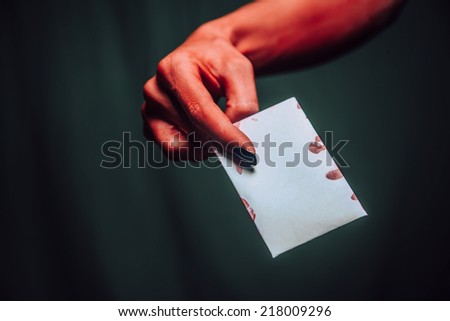 Red devil or demon hand gives empty card on dark background, space for text. Halloween or horror theme