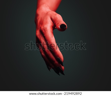 Red demon hand with handshake gesture on dark background. Deal with the Devil. Halloween or horror theme