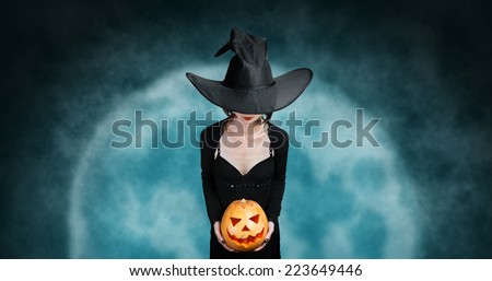 Witch holds Halloween carved pumpkin on background of full moon. Halloween, horror theme