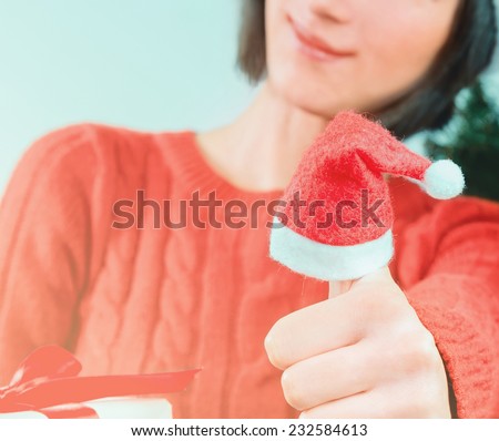 Smiling woman shows thumb up sign, thumb wearing in santa hat. Christmas or New Year celebration