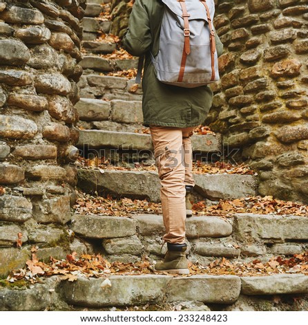 Unrecognizable woman with backpack walking up the old stone staircase in autumn outdoor, view of legs