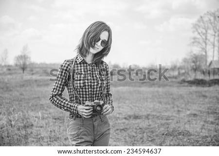 Happy hipster girl with vintage photo camera on nature. With film grain and low contrast effect. Black-white photo.