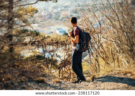 Young hiker man with backpack looking back in autumn outdoor in highlands. Hiking and recreation theme