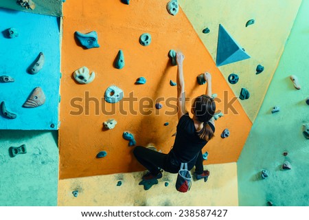Young woman climbing up on wall in gym, rear view