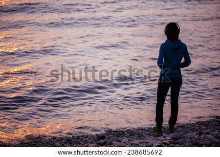 Girl in headphones standing on beach near the sea and listening music, rear view