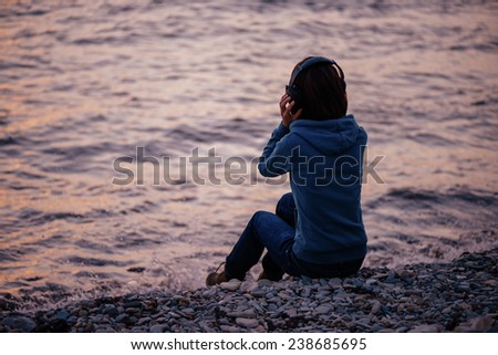Girl in headphones sitting on beach and listening music, rear view